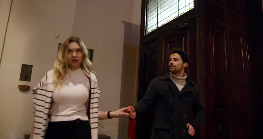 A couple holding hands is entering a large wooden door and looking around