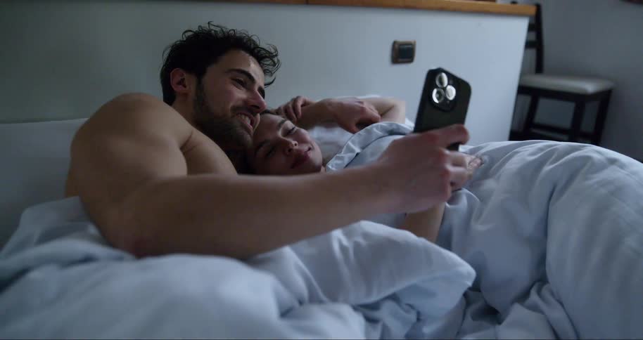 Couple lying together in bed interacting with a smartphone
