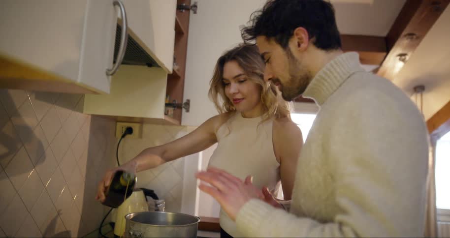 Woman putting oil in pan and man asking her to stop while they both cook in the kitchen