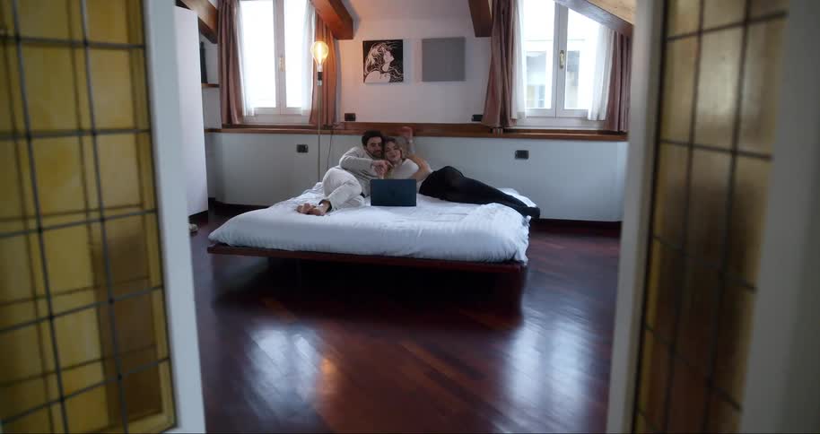 Couple lying together in bed with an open laptop