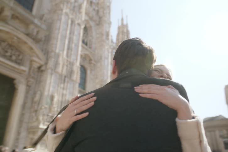 A young happy couple hug in front of a large ornate cathedral on a sunny day