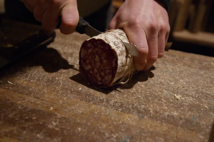 Slicing a large piece of salami on a wood cutting board