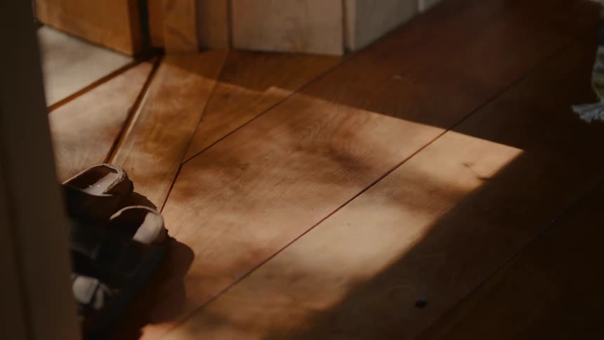 A pair of sandals in a doorway near the reflection of sunlight on the wooden floors
