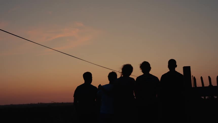 Five silhouetted figures stand against a gradient sunset sky with a thin wire diagonally crossing the frame