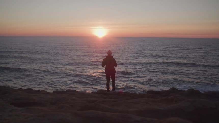 Silhouette of a person on rocky coast enjoying sunrise on seaside horizon