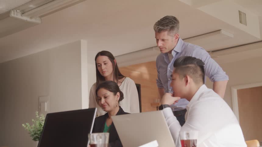 A group of office employees are collaborating while looking at a laptop screen