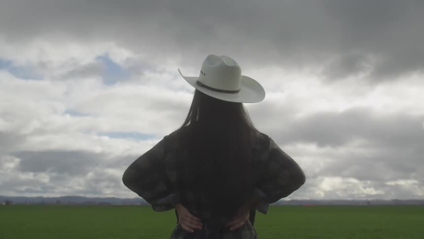 Woman wearing a hat and standing in a farm field with her hands on her hips