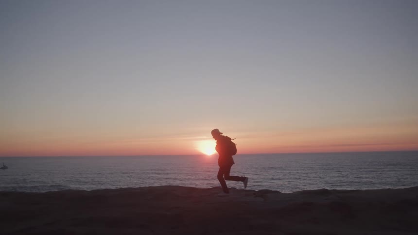 Silhouette of a traveler running on a rock by the sea with the sunrise on the horizon