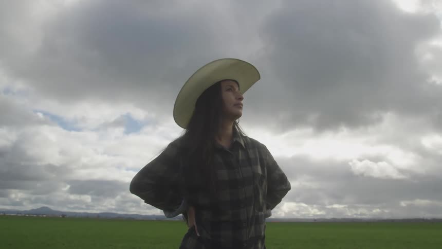 Thoughtful woman while wearing a hat in an agricultural field on a cloudy day