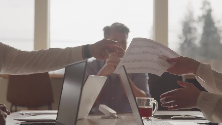 Several laptops open on an office desk and people talking and exchanging document papers