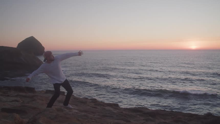 Man throwing a stone towards the ocean at sunrise