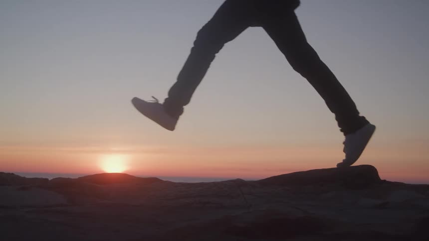 Backpacker runs at the coast while the sun sits on the horizon