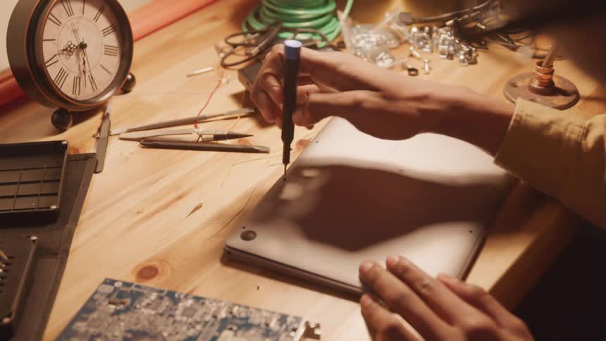 Close up of hand holding a screwdriver and unscrewing the back of a laptop on the table