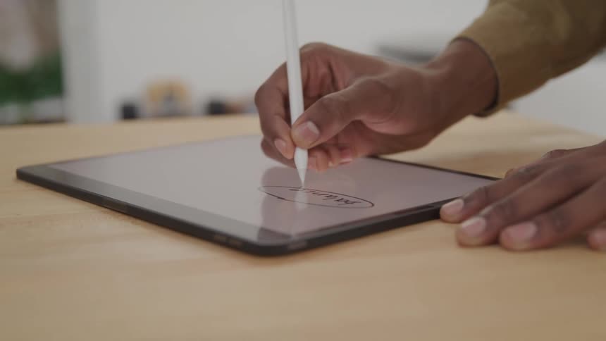 Hand with a digital pen drawing on a tablet on top of a wooden table