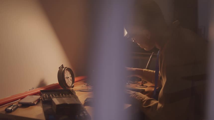 A young man sits at a desk and removes a screw from the back of an electronic tablet