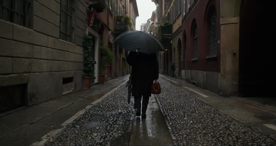Person walking with open umbrella down a hallway in a classic urban neighborhood