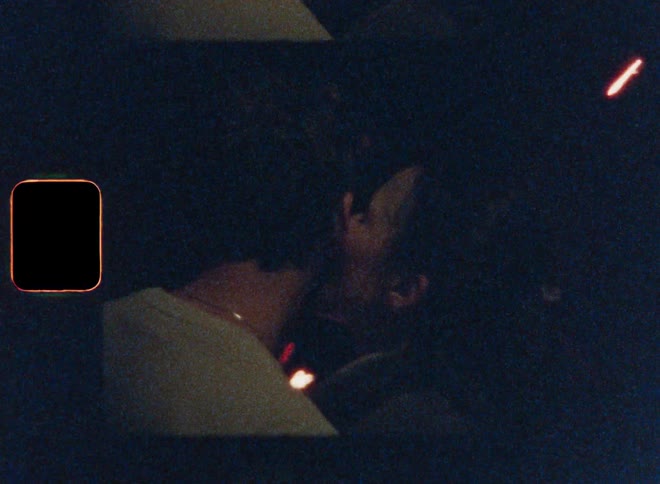 A woman kissing a mans cheek in a nighttime outdoor area with fireworks exploding in front