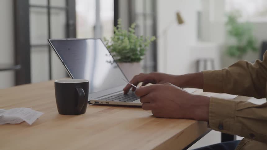 A person is using a laptop typing on the keyboard with one hand while holding a credit card in the other hand