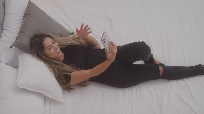 Female laying on bed face timing on her cell phone