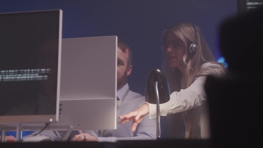 In a modern office one person talks to another at a desk suggesting a call center or tech support setting