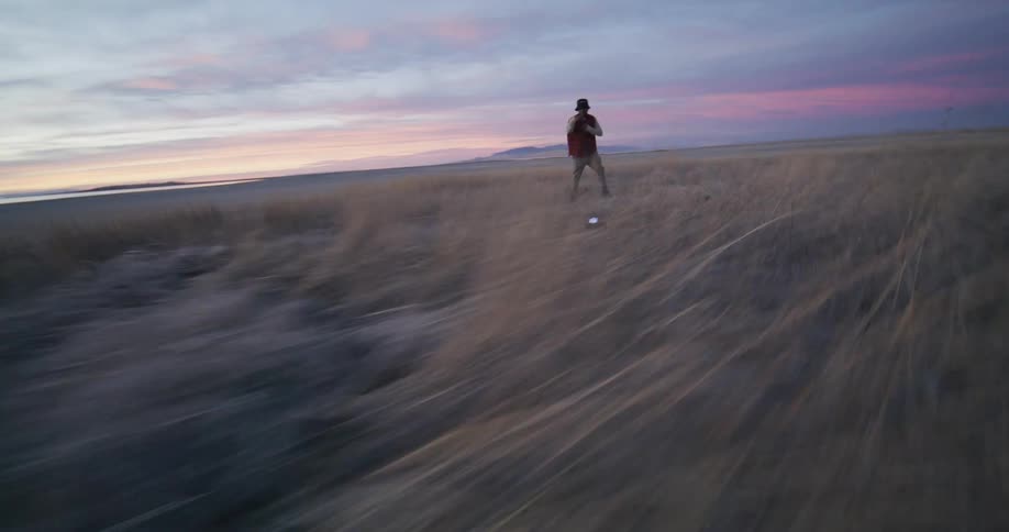An aerial view of a person dancing on a large field of white sand soil with some beige vegetation