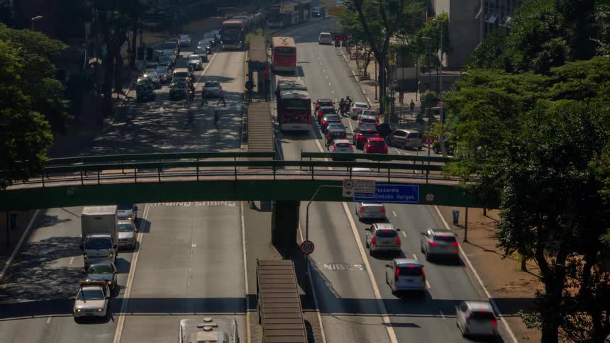 A busy highway filled with cars and trucks cuts through a city landscape dotted with trees