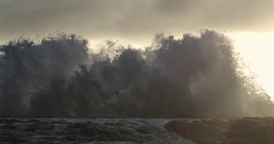 Waves crash against the rocks in the sea with the soft sunlight in the background
