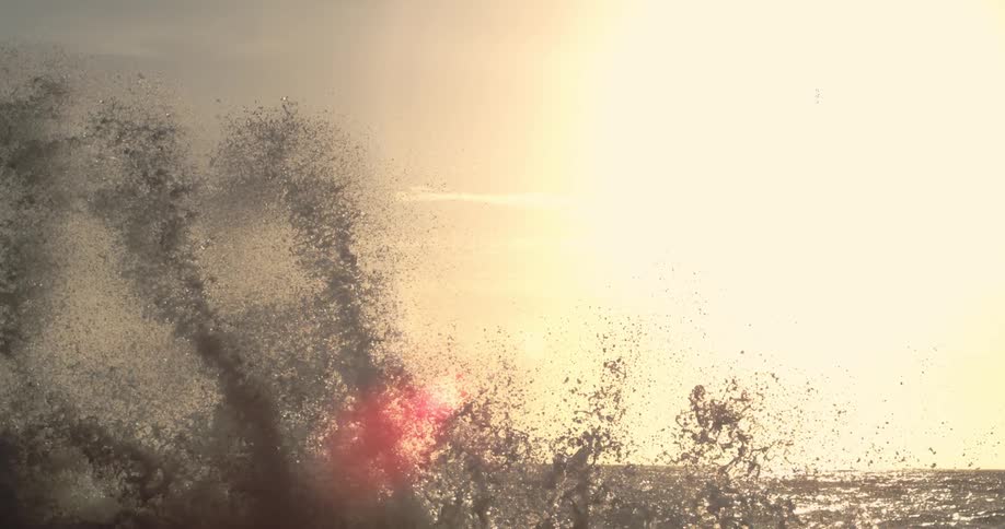 Waves crash against the shore with the sunlight creating a golden effect in the background