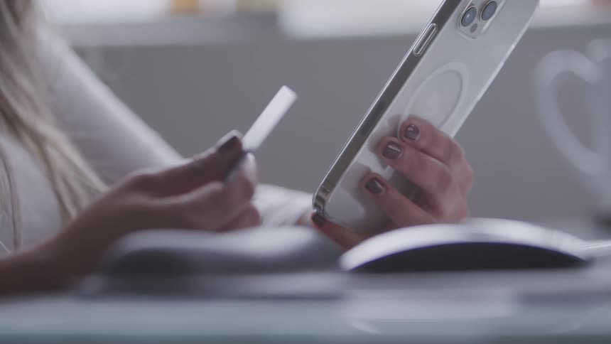 A person holds a credit card and a cell phone in their hands with a computer mouse visible on the desk