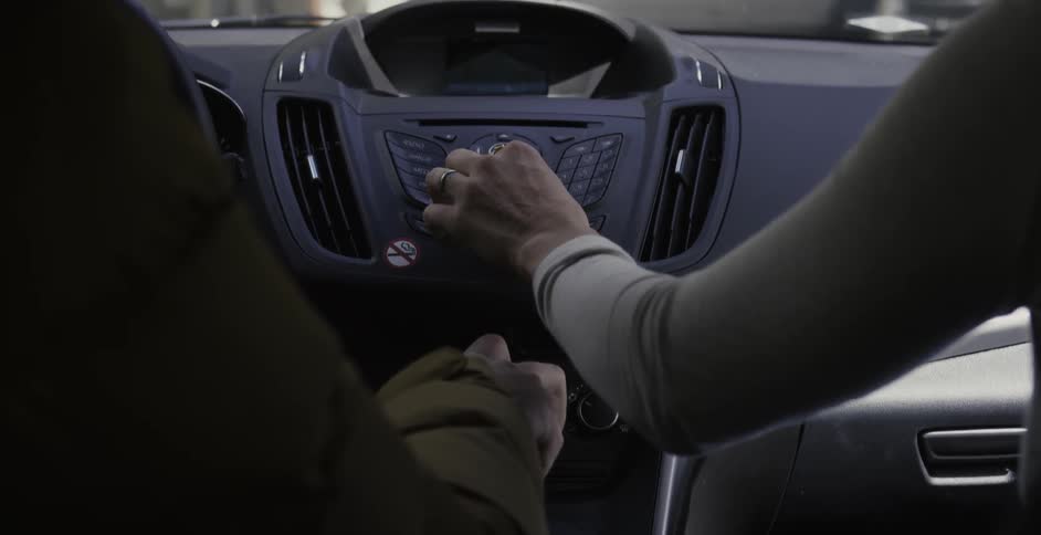 A car passenger reaches over and makes an adjustment on the dashboard