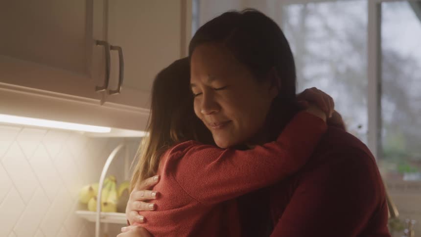 A woman is holding a little girl and hugging her as she smiles