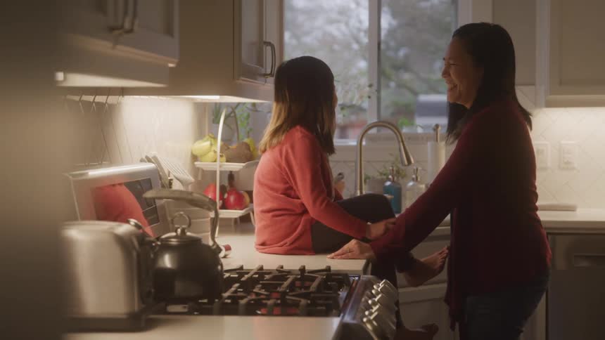Mother smiles and talks to her daughter while the girl sits on the kitchen counter