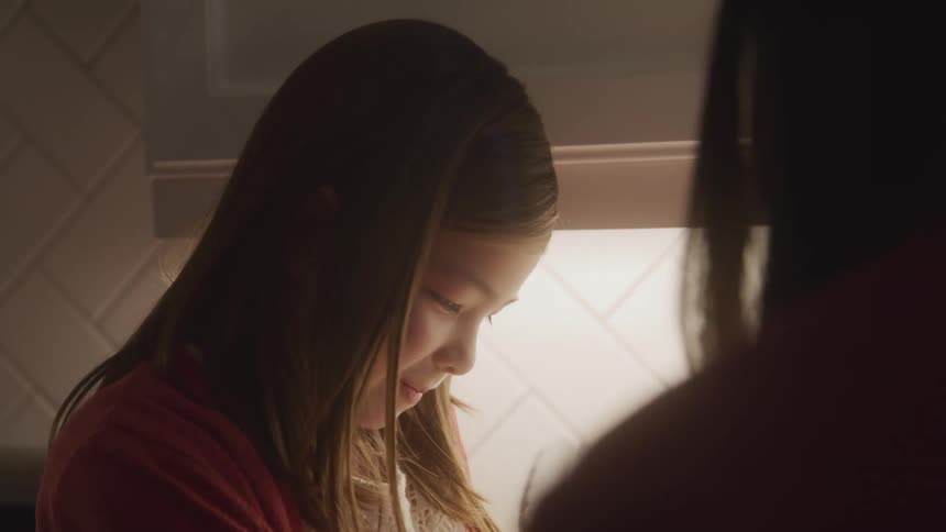 The face of a little girl who is looking down and then looks at someone who is next to her and smiles