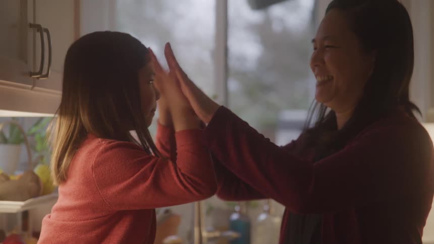 A mother and her daughter are having fun highfiving each other in the kitchen