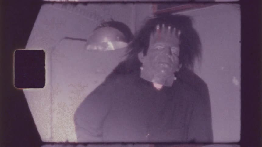 A person standing wearing a halloween mask in a partially dark indoor environment