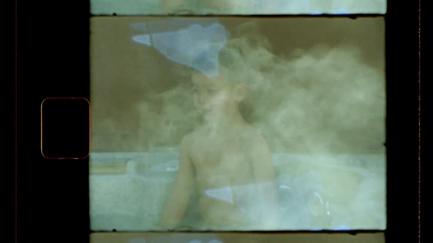 A vintagestyle shot shows a young person with short hair taking a bath on an outdoors hot tub