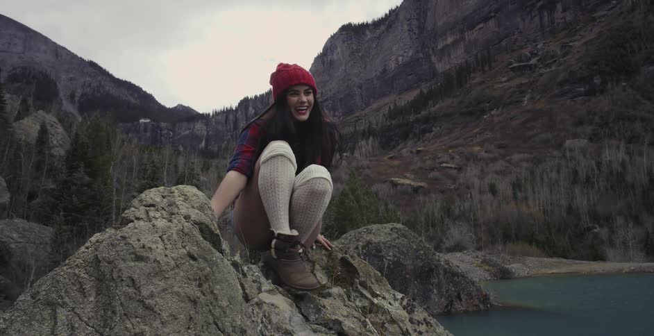 Woman in shorts and long socks smiling as she sits on top of a rock