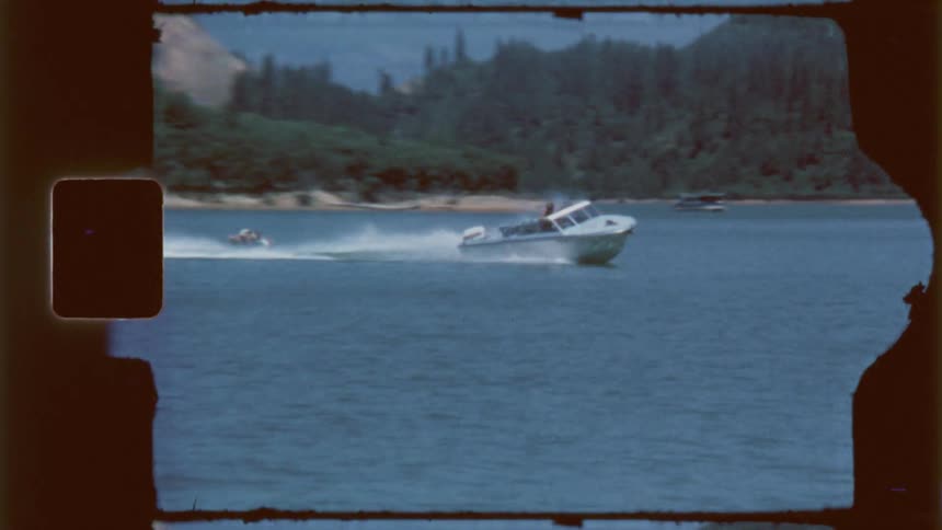 A speedboat races across calm water toward a distant shoreline pulling people on a large inflatable tube