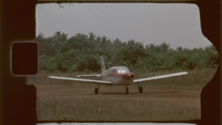 A small white and red single engine plane is preparing to take off on a runway near vegetation