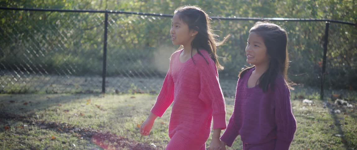 Two girls hold hands and walk in a park