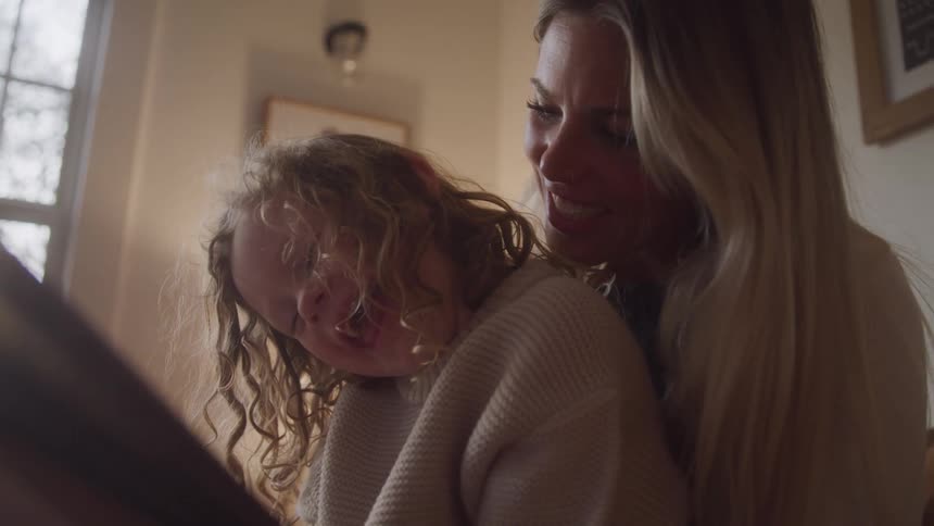 Mother and daughter are smiling as they look at a book together sharing a moment of joy
