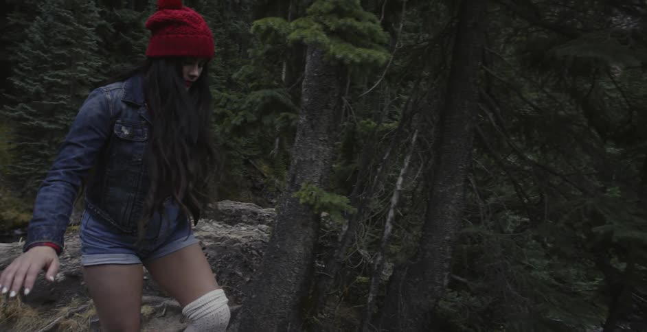 Woman in jean jacket steps carefully through forest