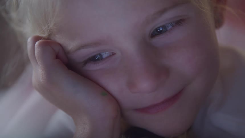 Portrait of a little blonde girl with a happy facial expression looking at a screen