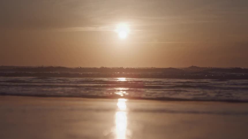 The sun reflects off the wet sand and into the ocean with soft waves during a golden hour at the beach