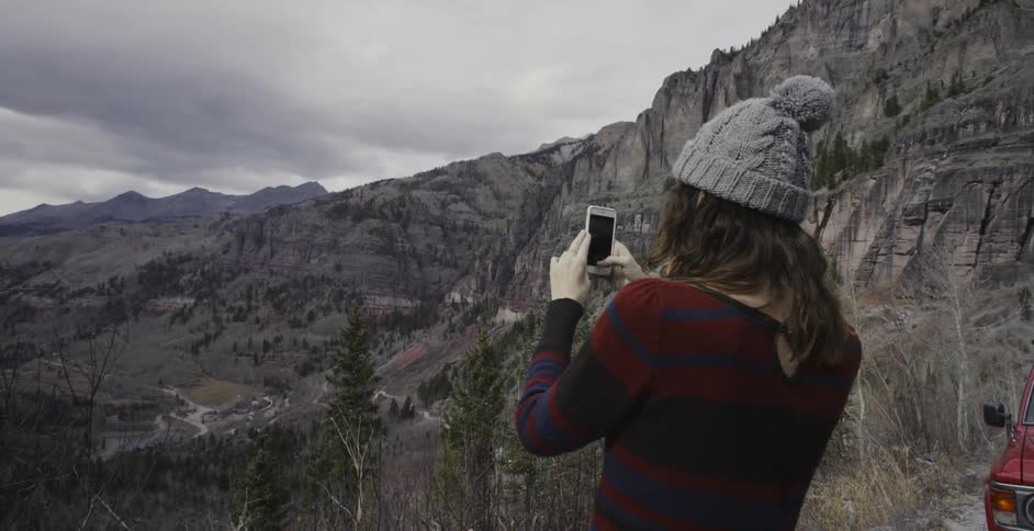 Woman takes a picture of mountainous landscape with her cell phone