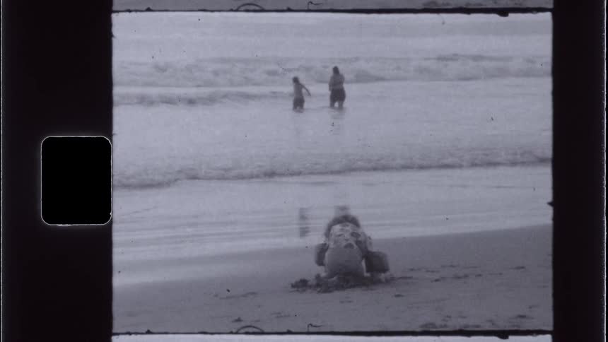 Girl digs in the sand while her sister and mother wade into the surf on a misty day