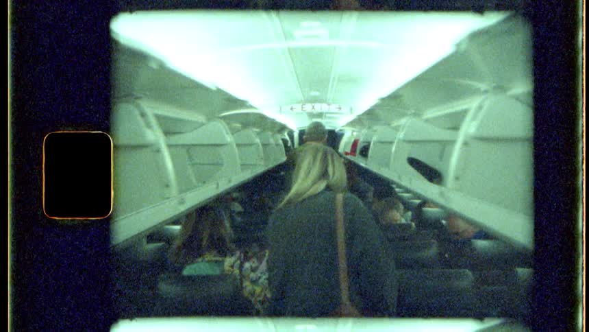 A woman walks down the aisle of an airplane where other passengers are seated