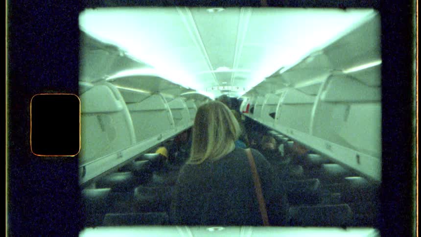 A vintagestyle shot shows a person with long blonde hair walking down the aisle of an airplane away from the camera
