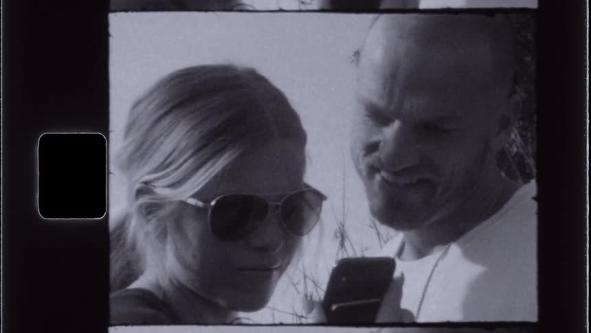A vintagestyle shot shows two people looking at a smartphone screen with one person wearing sunglasses and the other smiling