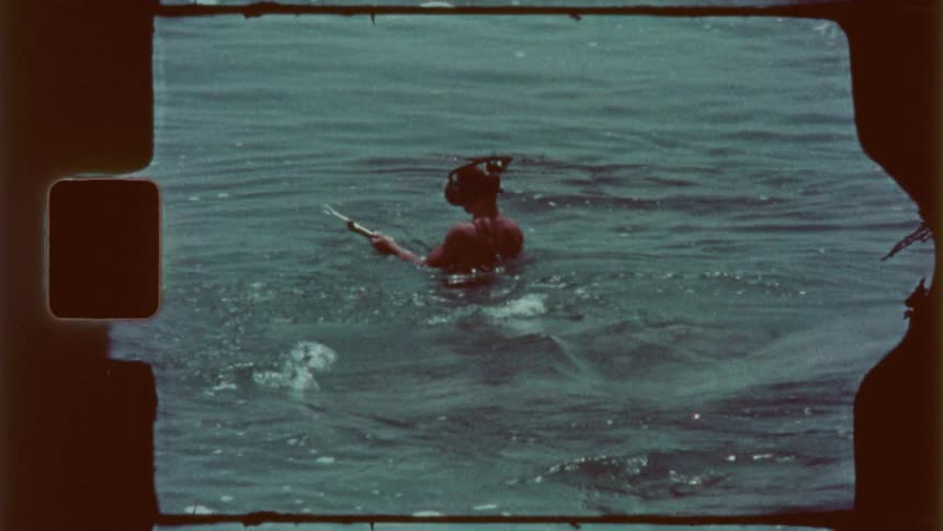 Male snorkeler holds a speargun while moving through the water near large rocks